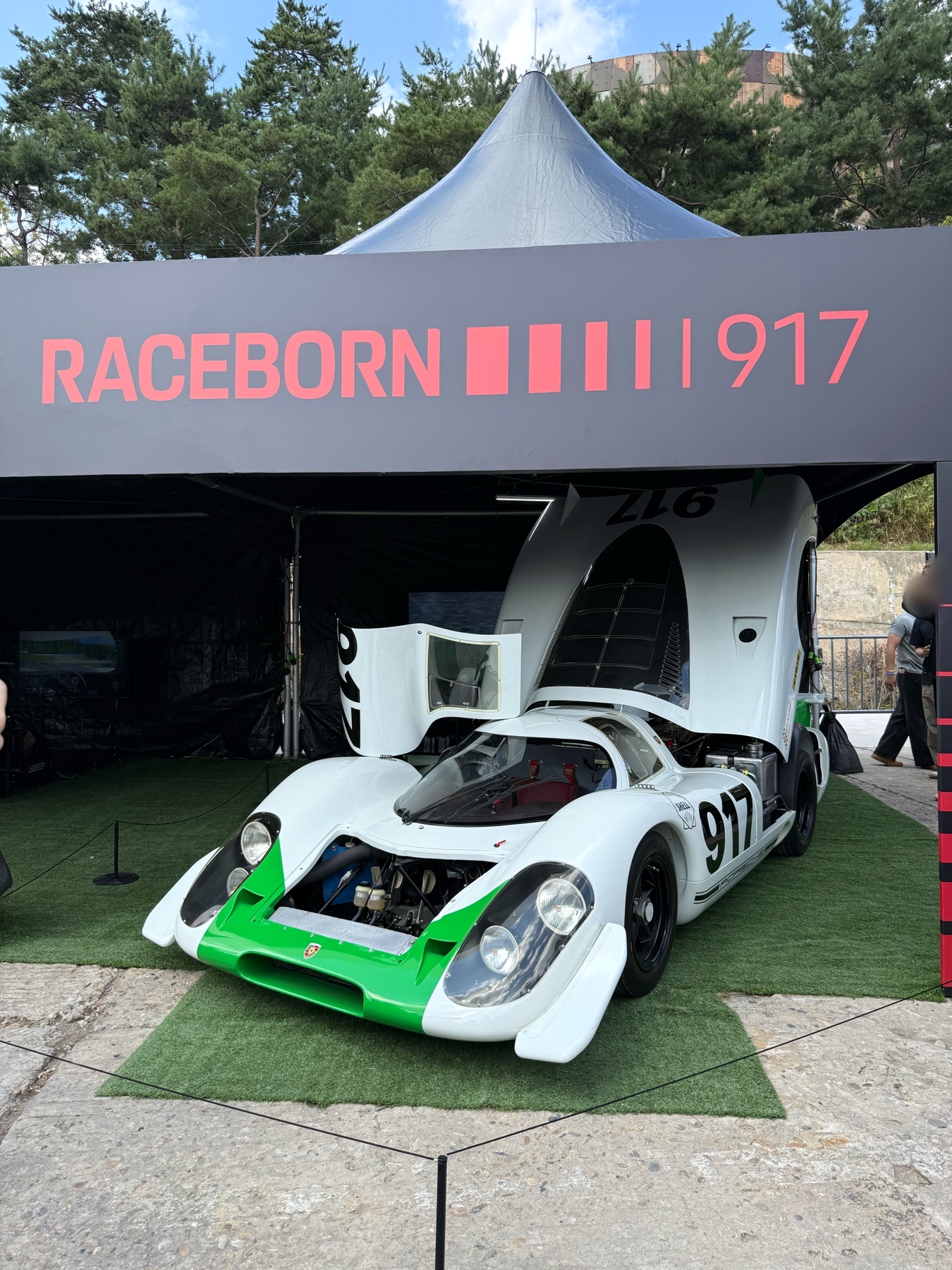 RACEBORN 917 안내판 아래 앞부분 일부와 뒤쪽 차체가 열린 흰색·초록색 전시 차량.